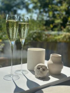 Two glasses of champagne against a hedge with three pots to the right made out of clay.